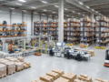 Interior de almacén logístico moderno con estanterías y sistemas automatizados de clasificación.